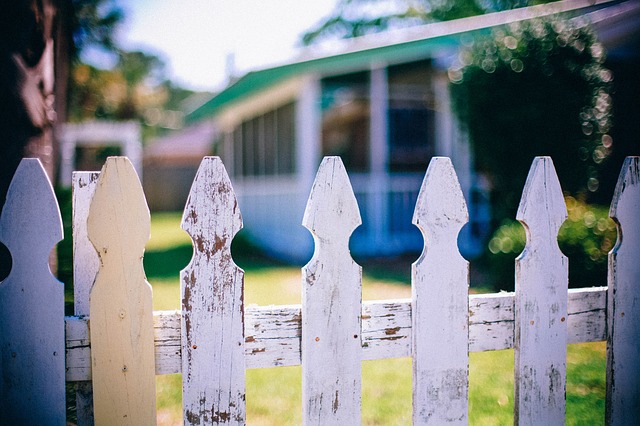 A white picket fence separating two hours through a yard.