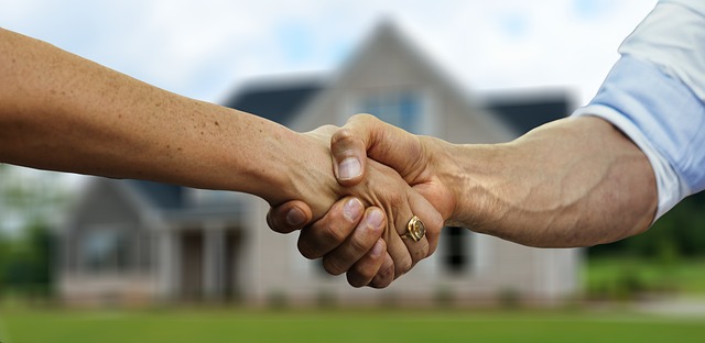A man and woman shaking hands in front of a house.