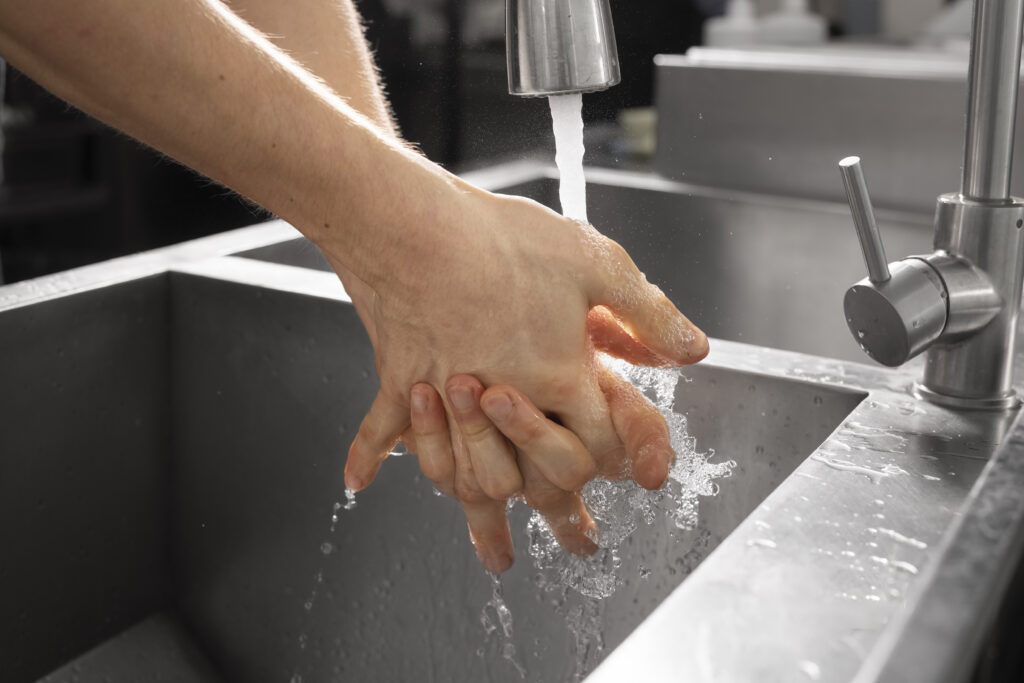 A close up of hands washing under a running water faucet in a restaurants kitchen sink. 