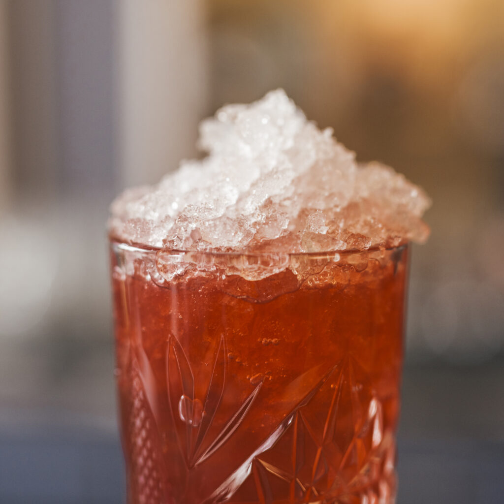 A red cocktail in a clear glass full of crushed ice. 