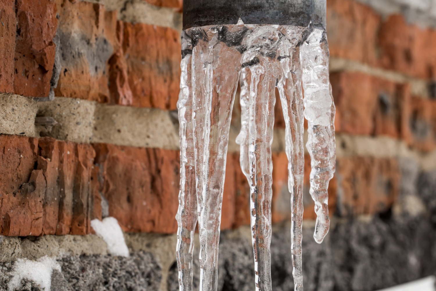 This outdoor drainage pipe is clogged with frozen water, creating hanging icicles which could risk causing frozen pipe disasters.