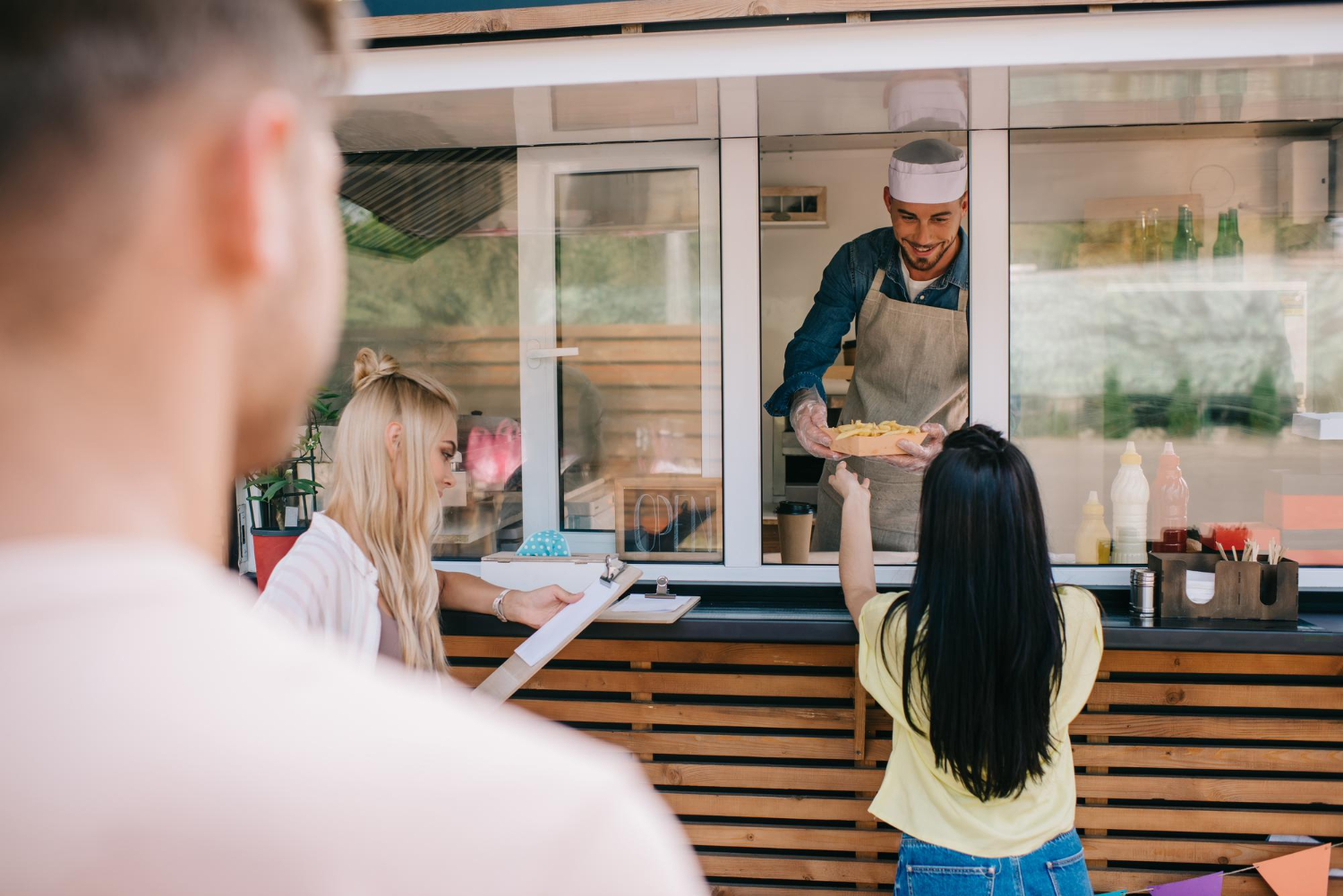 Customers receive their food orders and read the menu at a food truck service window.