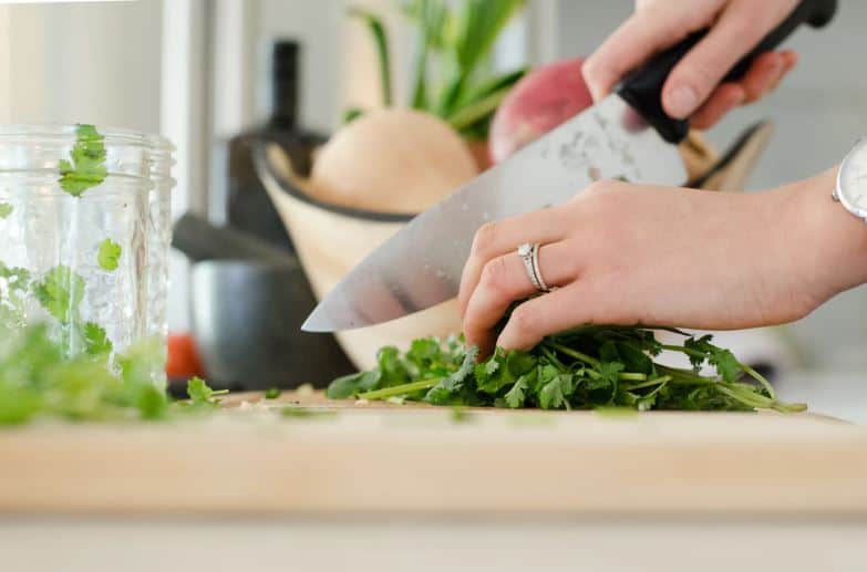Woman's hand chopping cilantro on a cutting board.