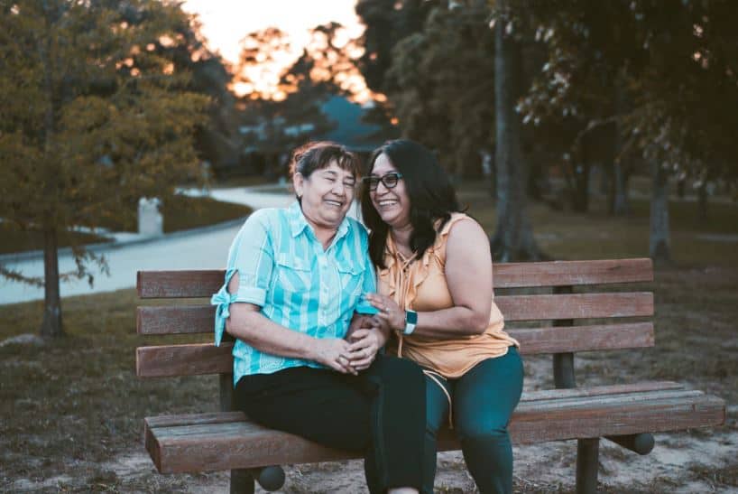 An older woman and her daughter sitting on a bench, laughing with each other.