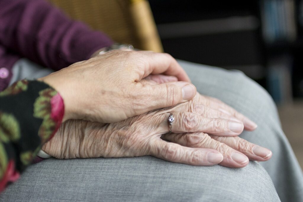 An older woman puts her hand on an older man’s hands as they rest in his lap. You can make the transition to assisted living easy with these tips