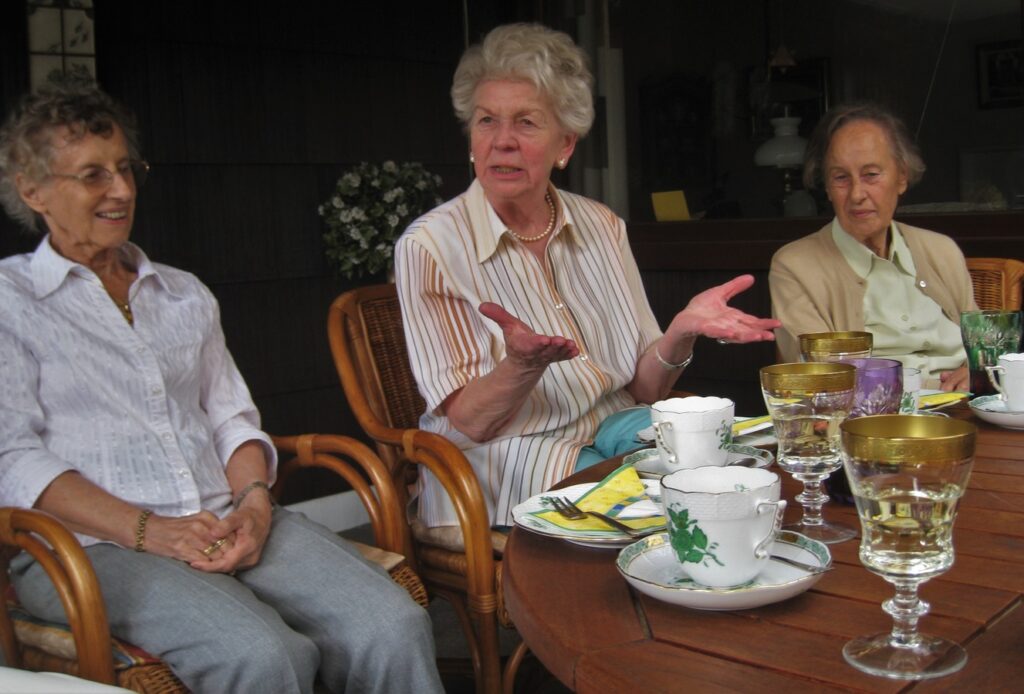 Three older women sit around a table having tea and talking. Social activities are one way to help seniors transition to assisted living facilities. 