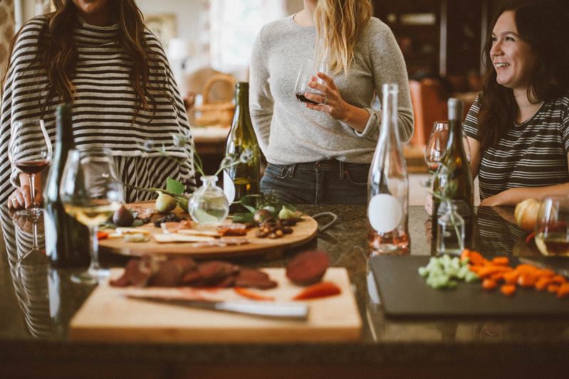 Three women drinking wine and sitting around a restaurant table with appetizers