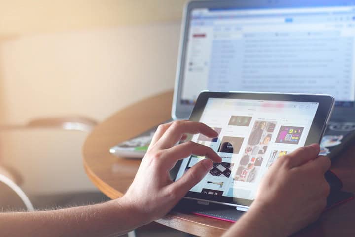 A woman’s hand pinches the screen of a touch-screen tablet while her laptop is open to her email on a table. Hotel smart technology includes the use of your guest’s mobile devices.