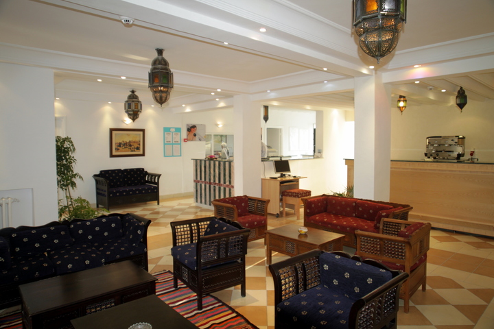 A clean, cozy guest area in the hotel lobby has hanging lights, couches and chairs, and the front desk. 