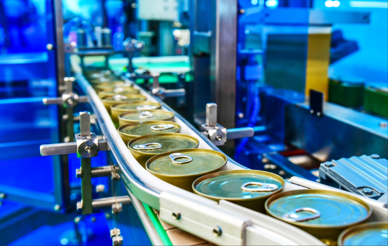 A line of canned goods travels down a conveyor belt at the food manufacturing facility.
