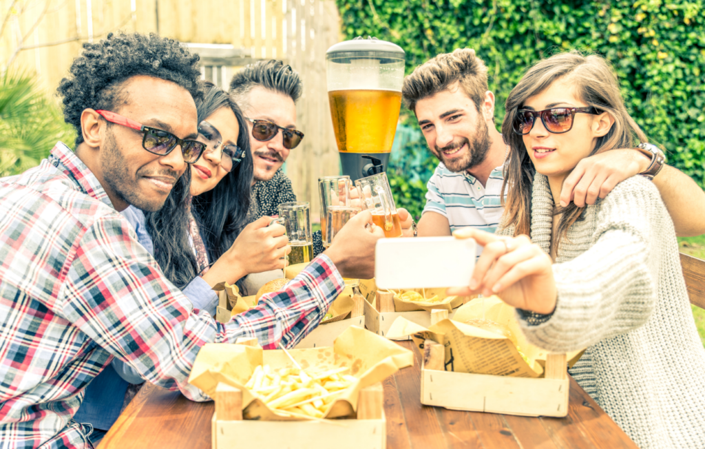 Friends enjoy beer and food while sitting at a picnic table in an outdoor beer garden. 