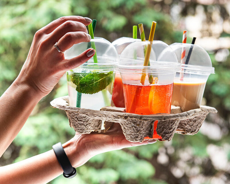 A woman's hand holds a drink tray full of colorful carryout cocktails.