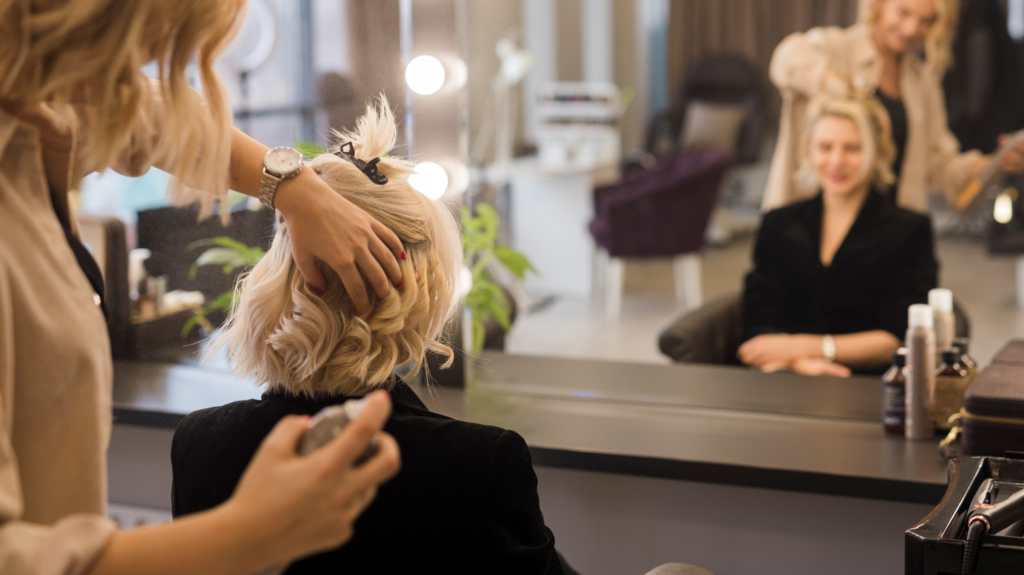 A woman is smiling into a mirror as she gets her hair styled at a salon and spa. 