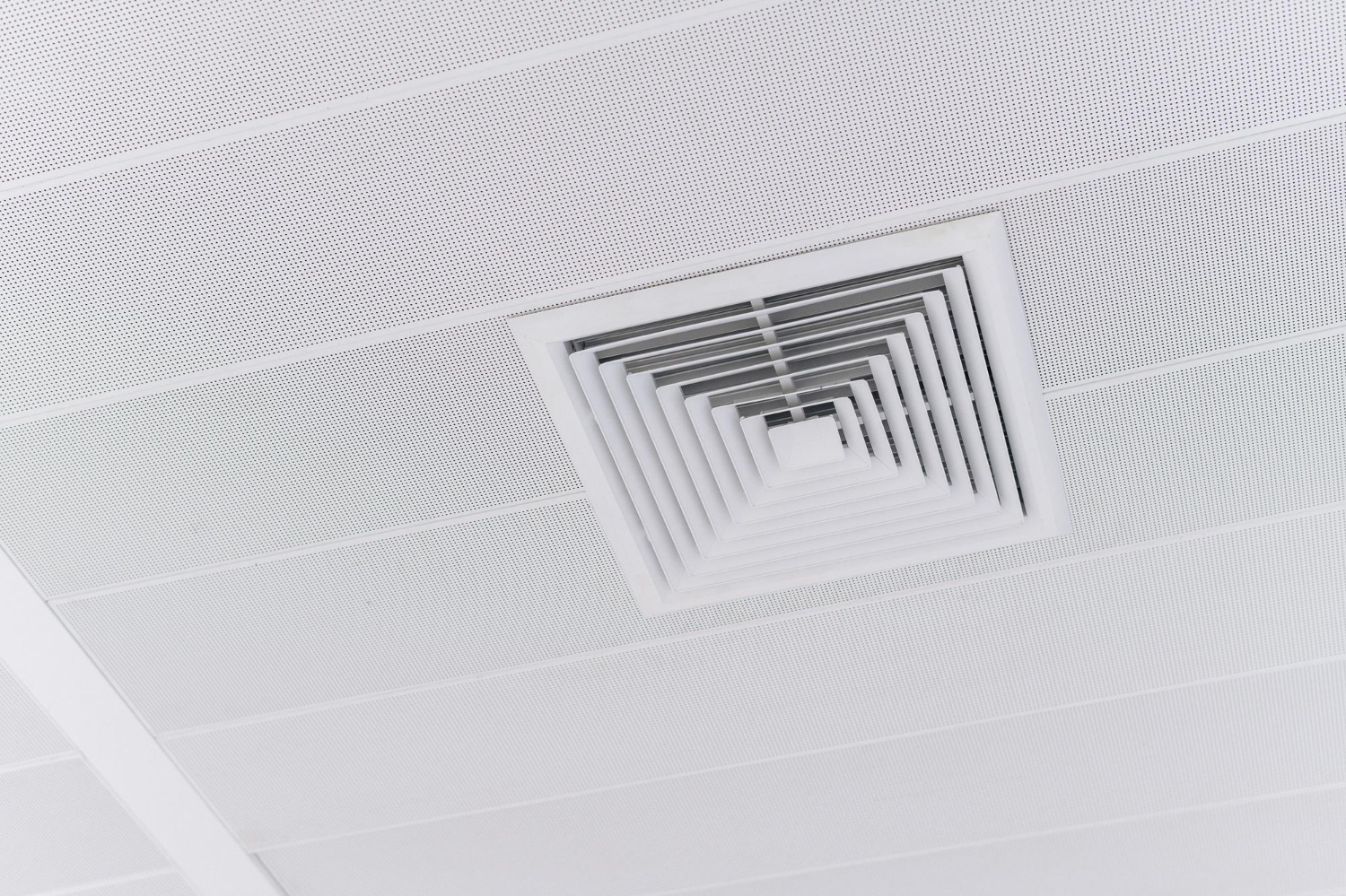 A white square ceiling air vent set into a white ceiling.