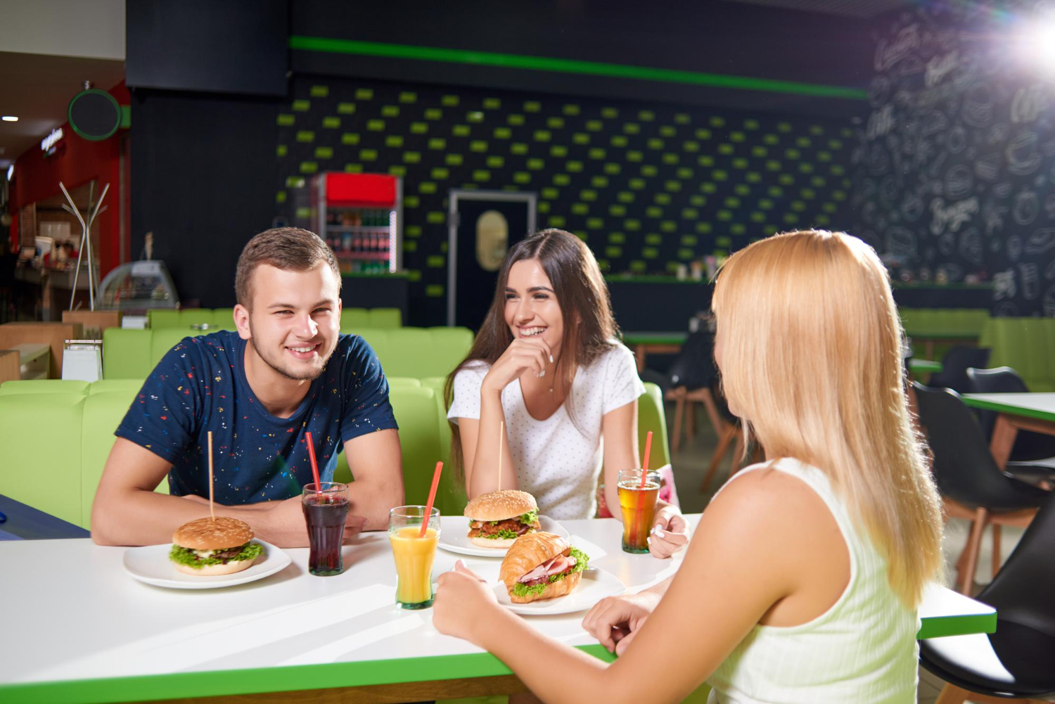 A man and two women sit at a booth at a fast casual restaurant, enjoying sandwiches and drinks while smiling and laughing with each other.