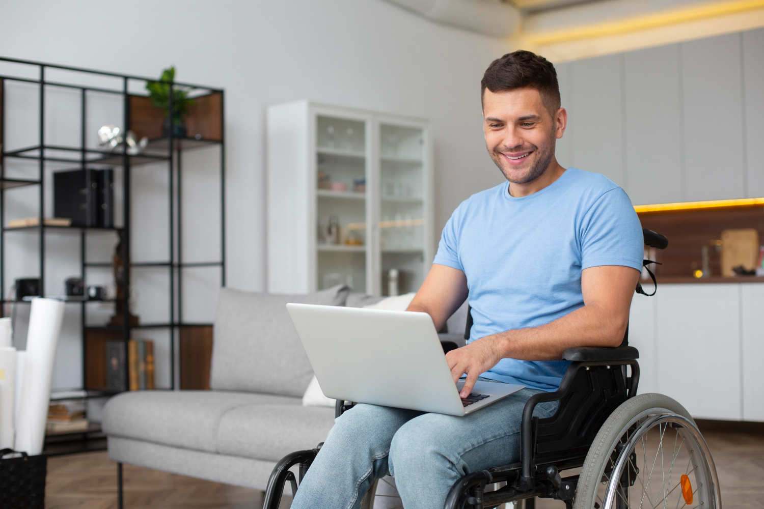 A young man in a wheelchair works on a laptop while sitting in the living room of his home.