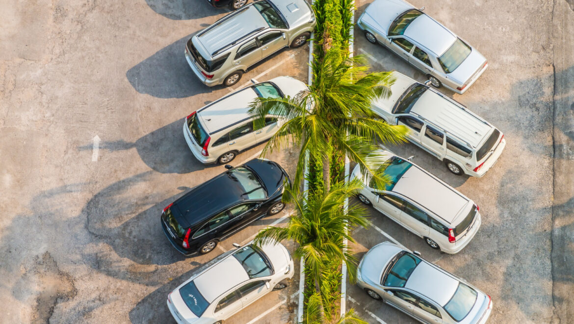 An aerial shot of two rows of diagonally parked cars in a parking lot. A median of green trees separates the two rows of cars.