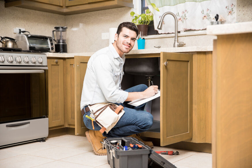 An attractive handyman kneels by the sink while writing an estimate. 