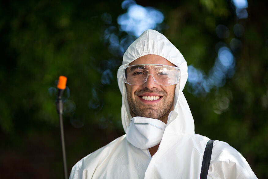 A smiling eco-friendly professional exterminator stands with a pesticide spray, ready to aid hotels in bed bug prevention and removal. 