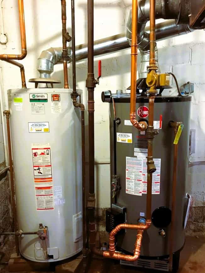 2 standard-efficiency gas storage water heaters with metal flues vented at top of units, an example of type of equipment that will not longer be built after Oct 2026